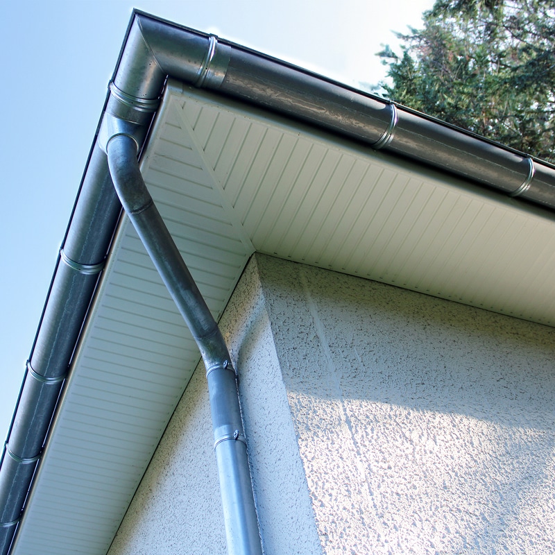Gouttière et Descente d'Eau sur Façade Crépis Gouttière en zinc et descente d'eau pluviale sur le coin d'un bâtiment avec soffite blanc et façade crépie.