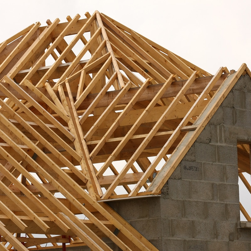 Charpente en bois d'une maison en construction, avec murs en parpaings apparents et ciel clair.
