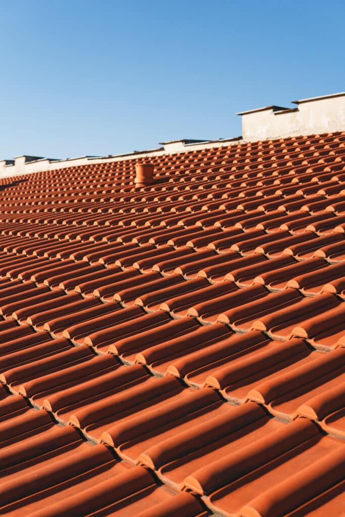 Toit en tuiles rouges sous ciel bleu : architecture extérieure Toit en tuiles canal rouges courbes sous un ciel bleu clair et ensoleillé, avec une cheminée visible.